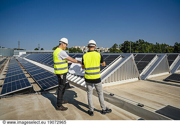Two technicians discussing plan on the roof of a company building with solar panels