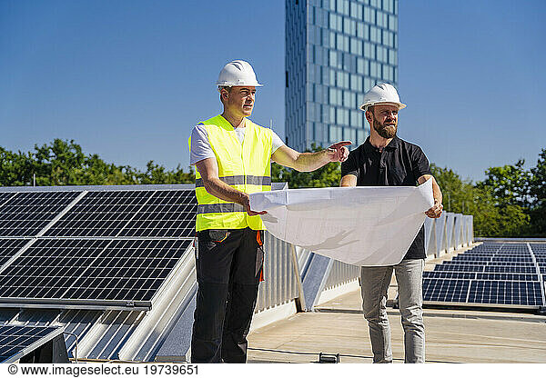 Two technicians strategizing on the rooftop of a corporate building adorned with solar panels