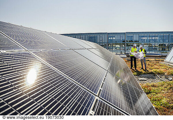 Two technicians studying plan on the roof of a company building with solar panels