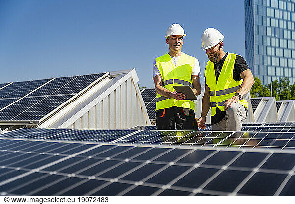 Two technicians using tablet PC on the roof of a company building with solar panels
