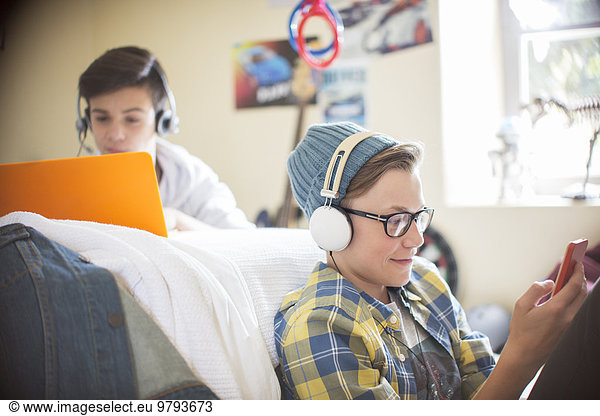 Two teenage boys using electronic devices in room