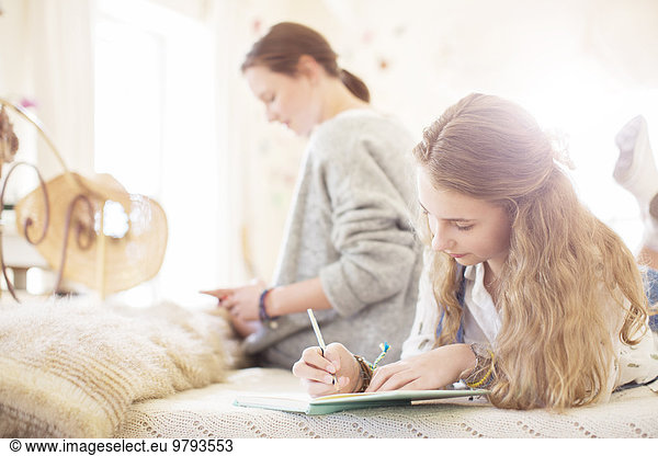 Two teenage girls on bed writting in notepads