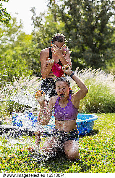 Two teenage girls wearing swimwear playing with water balloons in a garden.