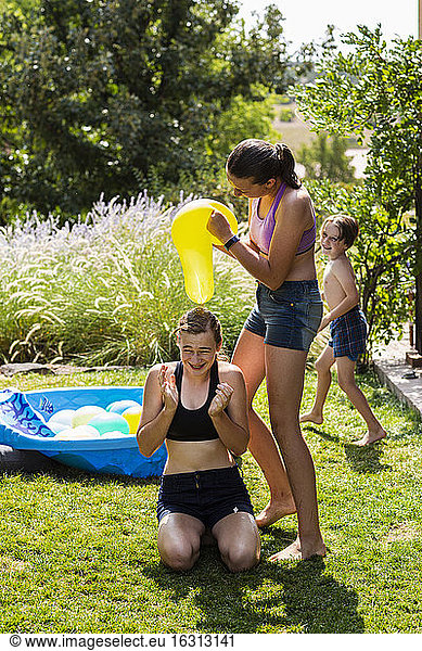 Two teenage girls wearing swimwear playing with water balloons in a garden.
