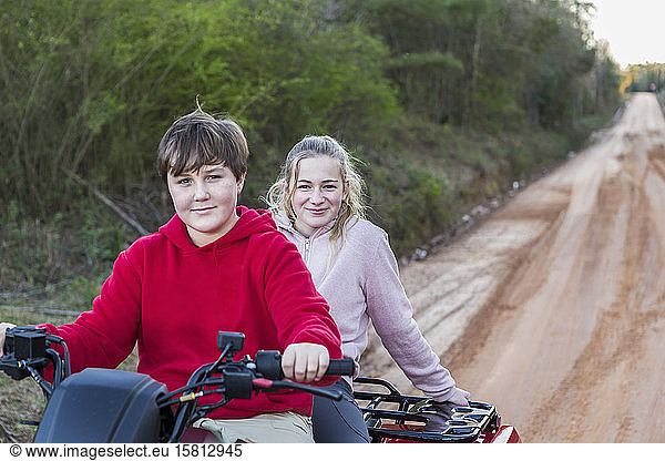 Two teenagers riding on a buggy  all terrain vehicle on a muddy track.