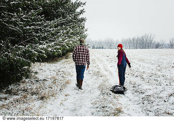 Two Teens Walking Through a Snowy Field with Pines in Michigan