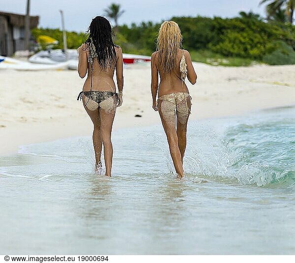 Two topless models walk on a beach in the caribbean