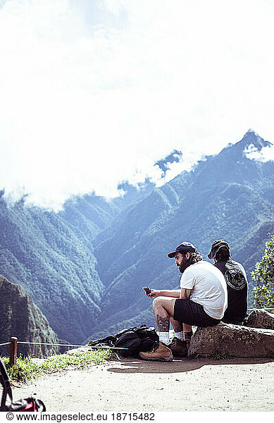Two traveller men sit and rest at top of Machu Picchu ruins