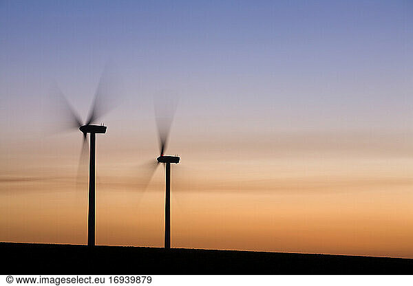 Two wind turbines turning  sunset sky