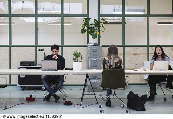 Two women and one man working at desk in creative office
