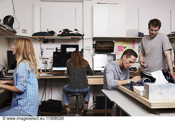 Two women and two men in a technology repair shop or lab  working on computers.