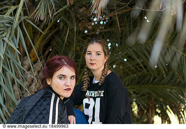 Two women are posing with palm trees in the background