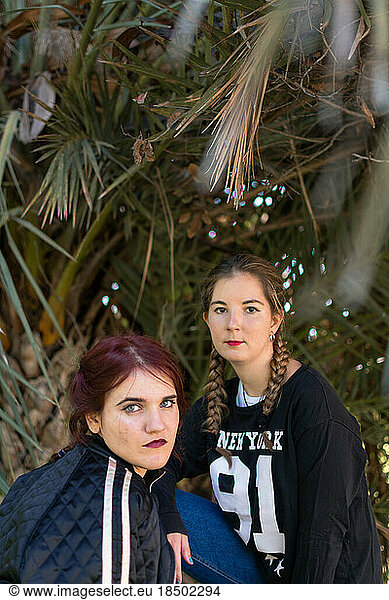 Two women are posing with palm trees in the background