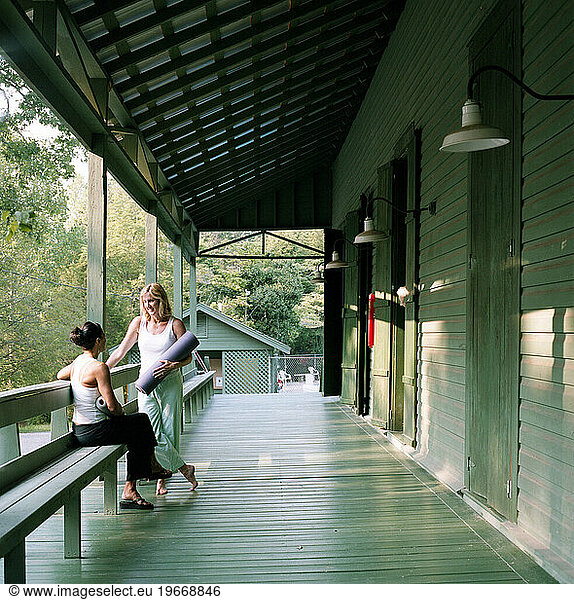 Two women chat outside an old wooden gymnasium before a yoga class.