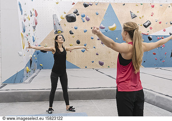 Two women doing stretching exercises before climbing on the wall