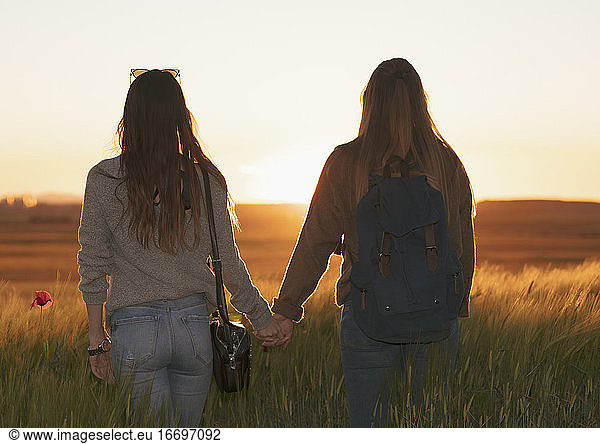 two women holding hands at sunset in the field