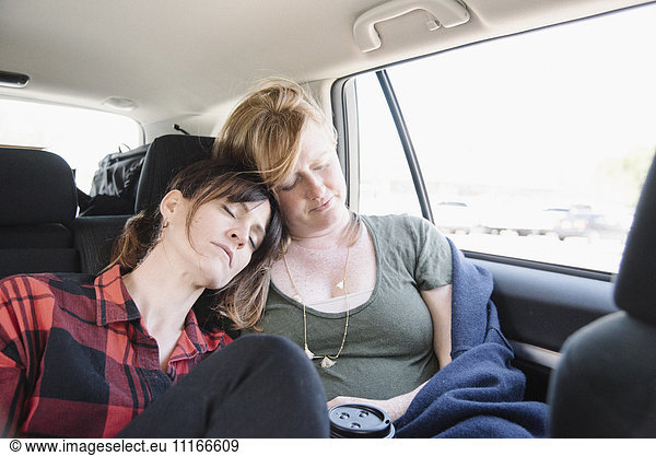 Two women in a car on a road trip  both asleep in the back seat  heads together.