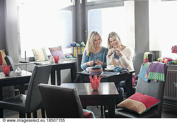 Two women knitting muffler and drinking coffee in coffee shop and smiling  Bavaria  Germany