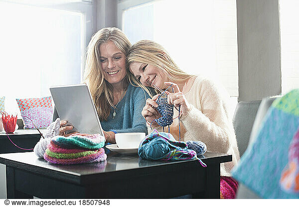 Two women knitting muffler and using digital tablet in coffee shop and smiling  Bavaria  Germany