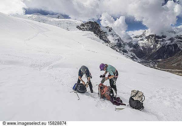 Two women mountaineers take a gear break on the Mera Peak glacier