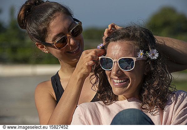 Two women outside laughing and putting flowers in hair.