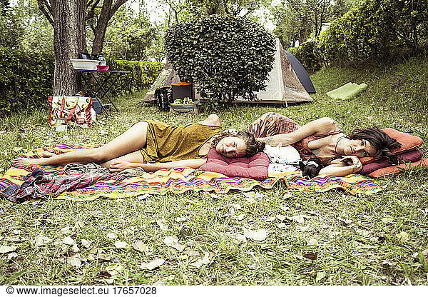 Two women relax together on grass in campsite in France