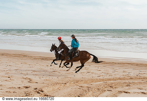 Two women riding Andalusian horses on the beach in Spain