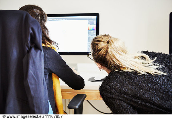 Two women seated sharing a computer screen and discussing the graphic content.