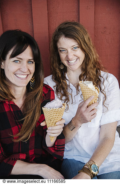 Two women sitting on a bench  eating ice cream.