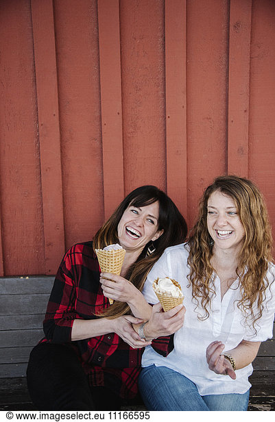 Two women sitting on a bench  eating ice cream.