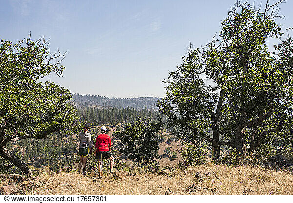 Two women stand at lookout over broad view of forests