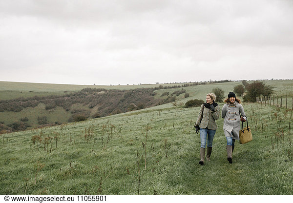 Two women walking on a country path across grassland.