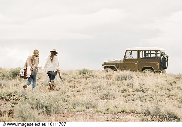 Two women walking towards a 4x4 parked in a desert.