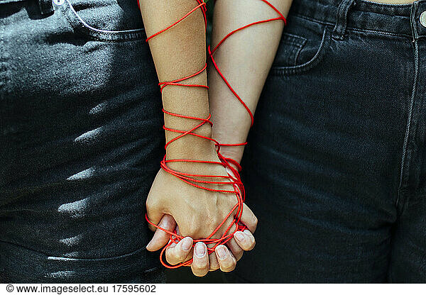 Two women with thread holding hands