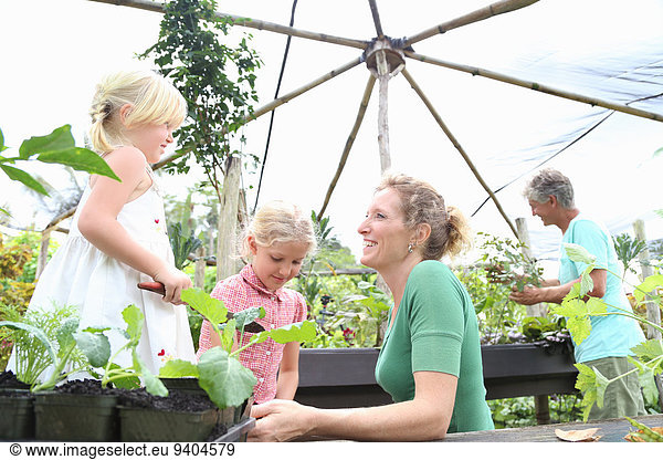 Two women working in greenhouse with girls