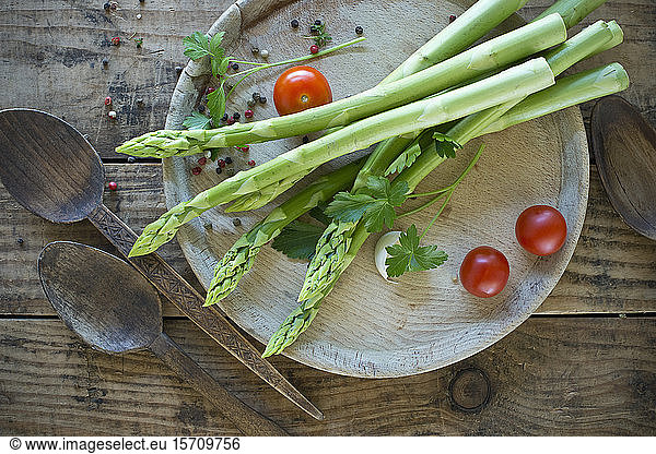 Two wooden spoons and tray with fresh asparagus  cherry tomatoes  parsley and pepper
