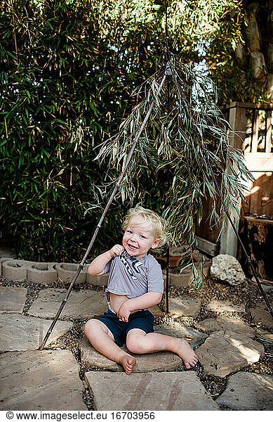 Two Year Old Boy Sitting Under Bamboo Laughing & Playing