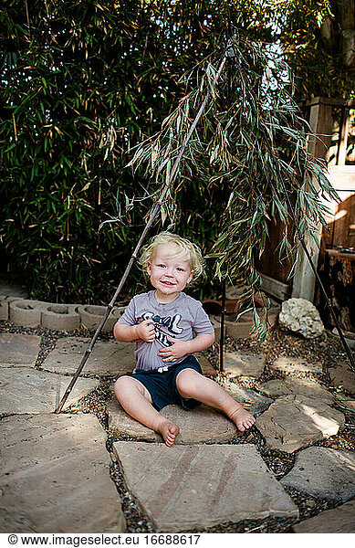 Two Year Old Boy Sitting Under Bamboo Smiling for Camera