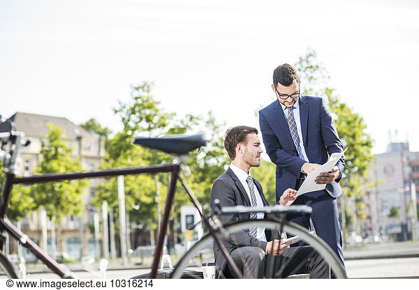 Two young businessmen discussing files outdoor