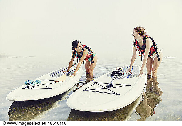 Two young female friends push their SUP boards onto shore at sunrise
