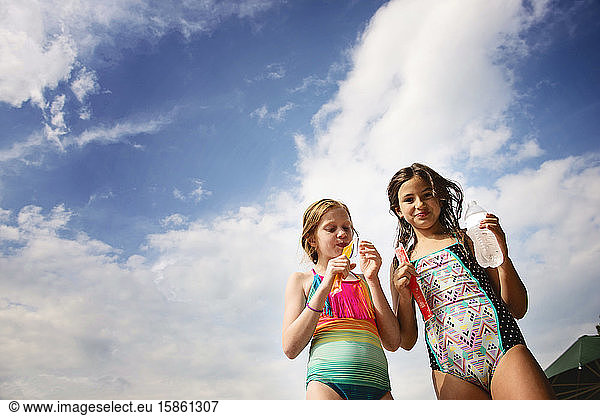 Two Young Girls in Swimsuits With Frozen Treats Against Blue Sky