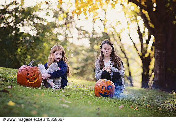 Two Young Girls Sitting Outside by Smoking Pumpkins in the Fall