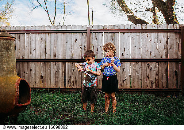 Two young kids standing in backyard covered in mud