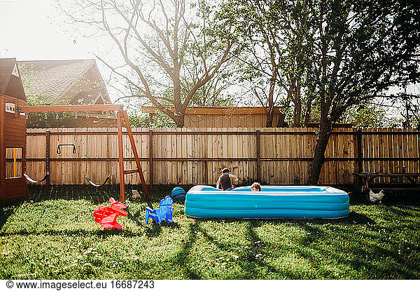 Two young kids swimming in backyard pool by swing set