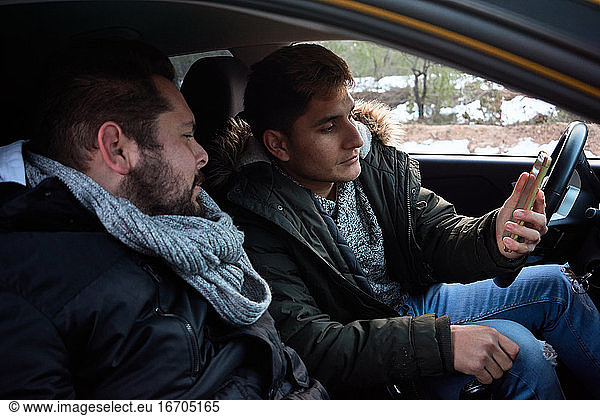 Two young men look at a phone inside a car. Concept of route finding