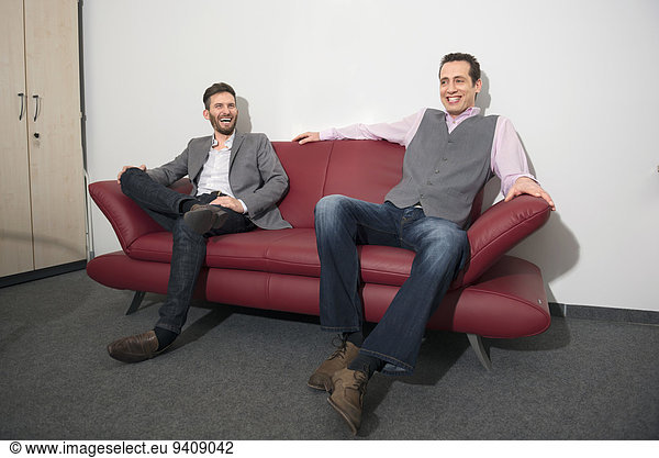 Two young men relaxing on office sofa waiting