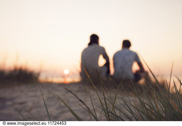 Two young men sitting on beach at sunset