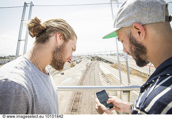Two young men standing on a bridge  looking at mobile phone.