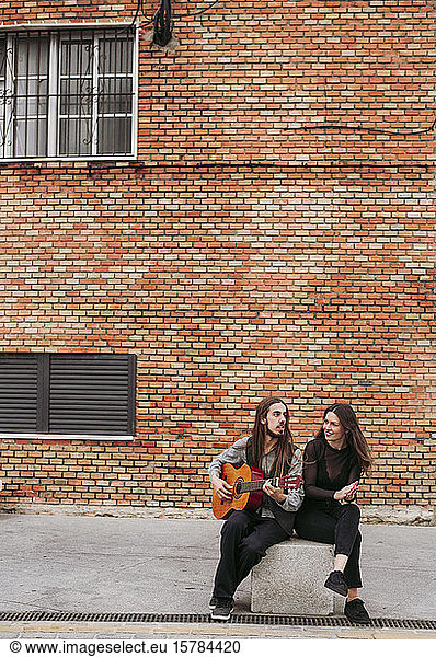 Two young musicians sitting on a stone playing guitar