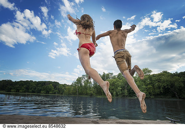 Two young people  boy and girl  running and leaping off the jetty into a lake or river.